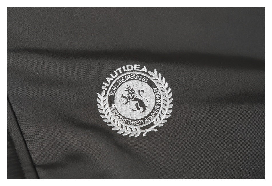 Close-up of a white embroidered circular crest with laurel branches on charcoal jacket fabric.