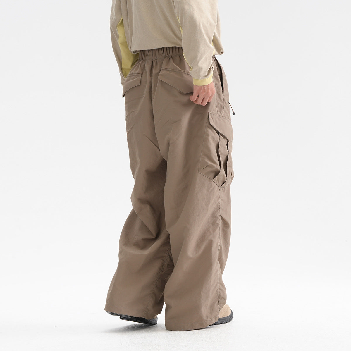 Rear three-quarter view of a model wearing loose taupe cargo trousers with an elastic waist and flap pockets.
