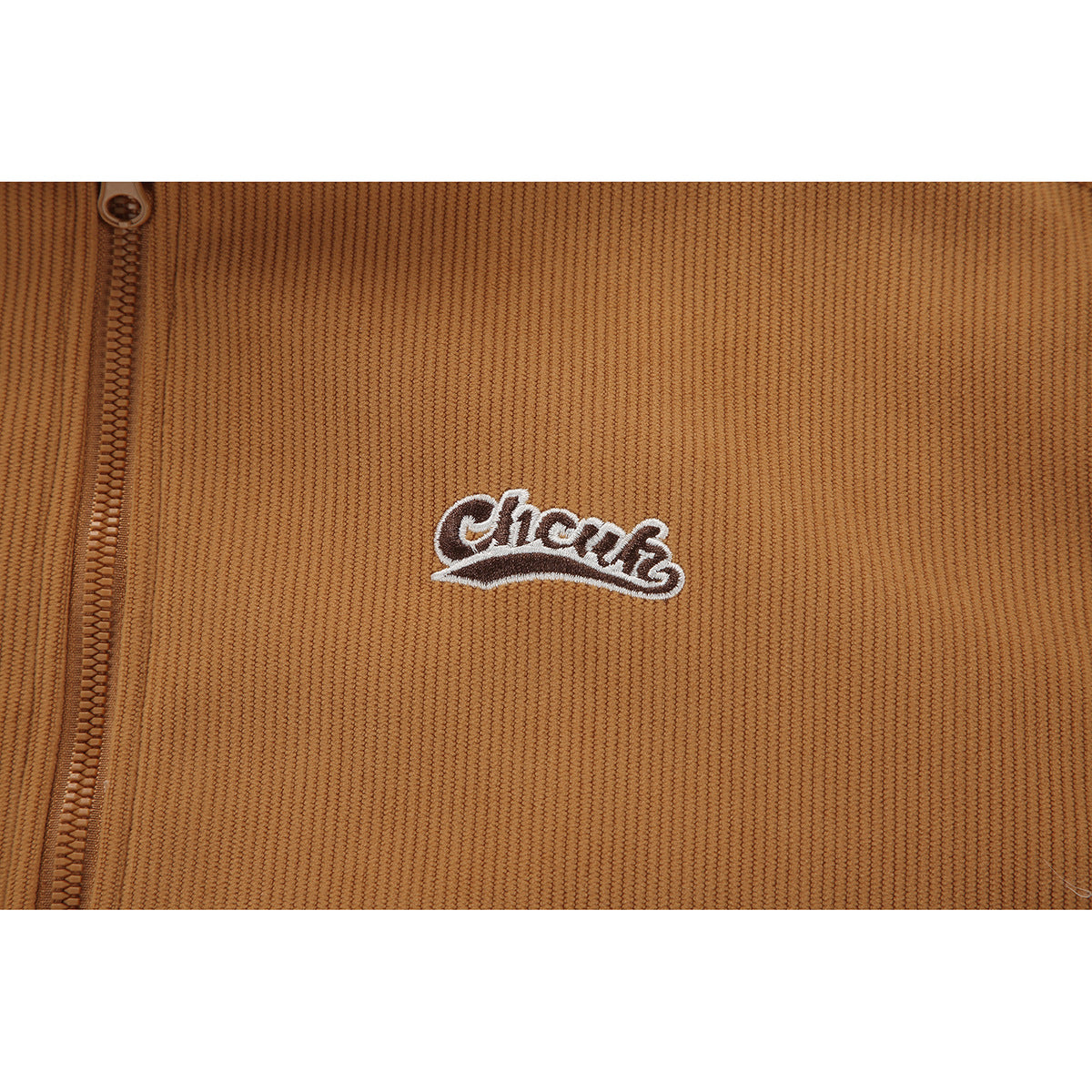 Close-up of a tan ribbed jacket showing its zipper and embroidered chest logo.