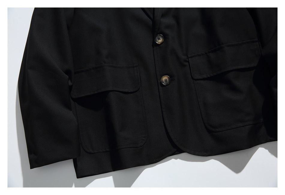 Close-up of the black blazer front showing two flap pockets and two dark buttons.