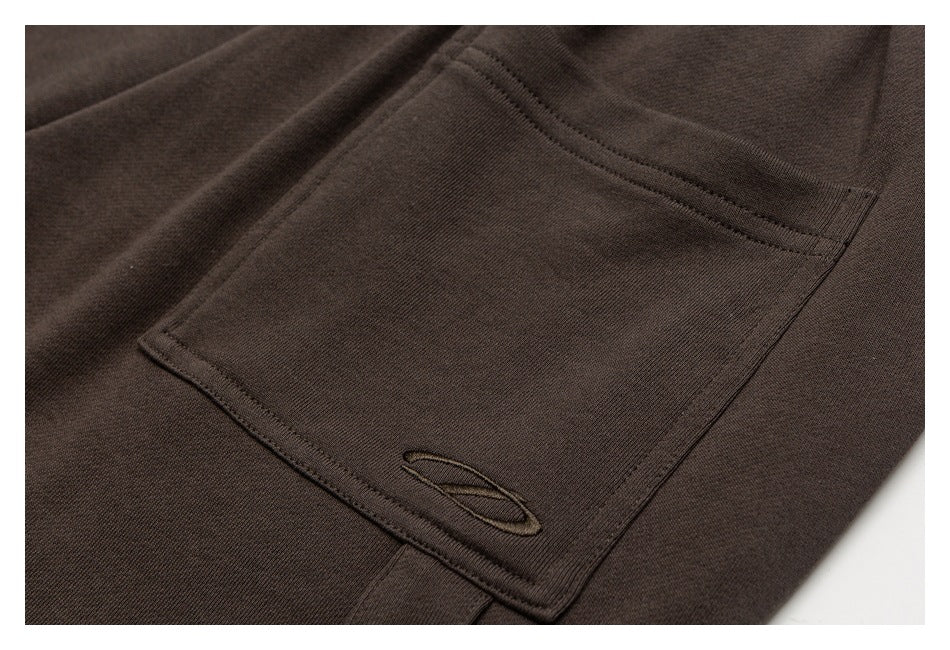 Close-up of a dark brown garment pocket with tonal stitching and a small embroidered oval emblem.