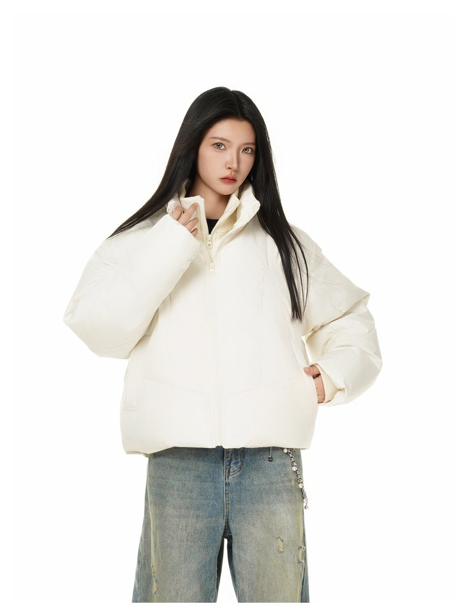 Woman wearing a cropped off-white puffer jacket with a stand collar, hand in pocket, styled with faded blue jeans