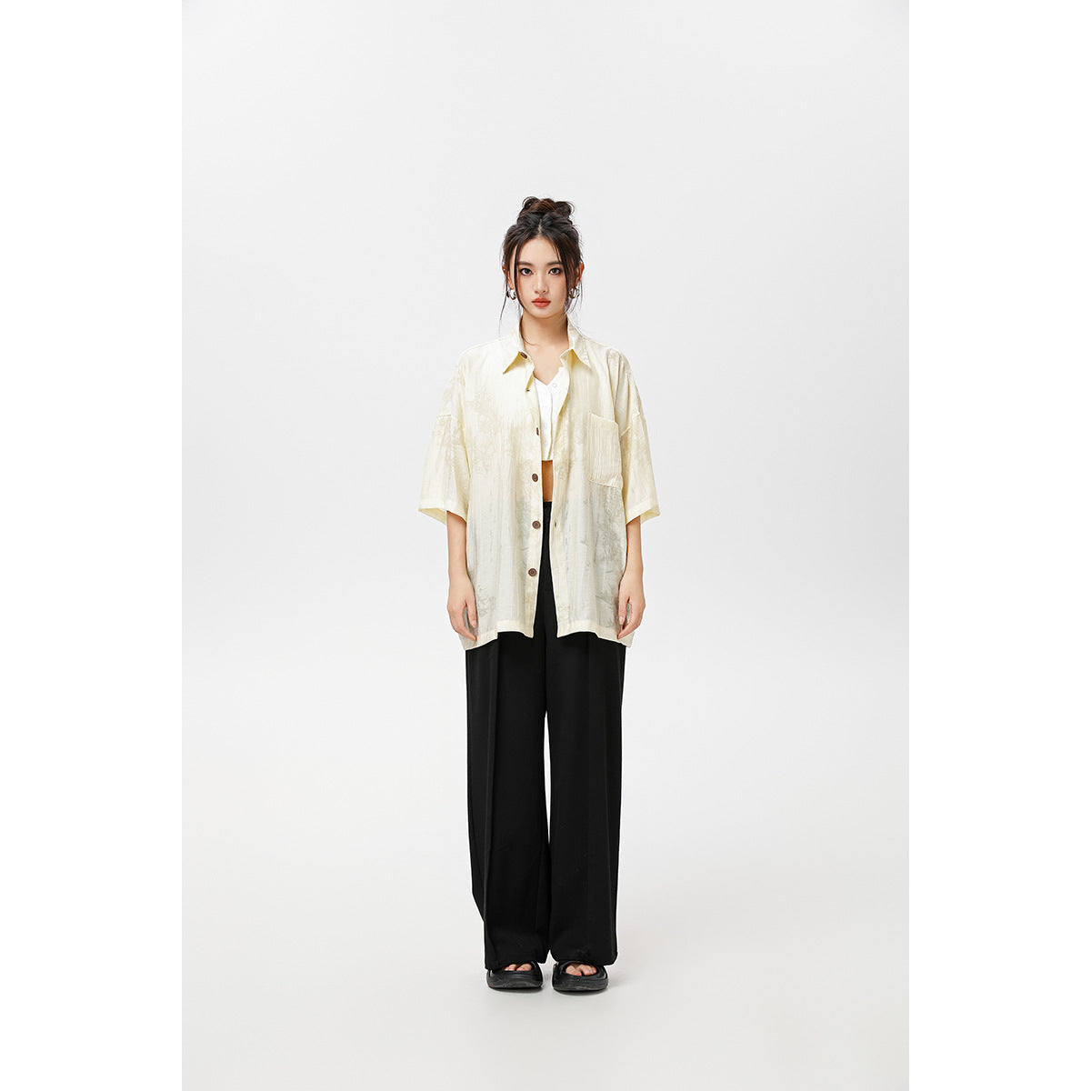 Model wearing an oversized ivory short-sleeve button-up shirt with a chest pocket and black wide-leg trousers.