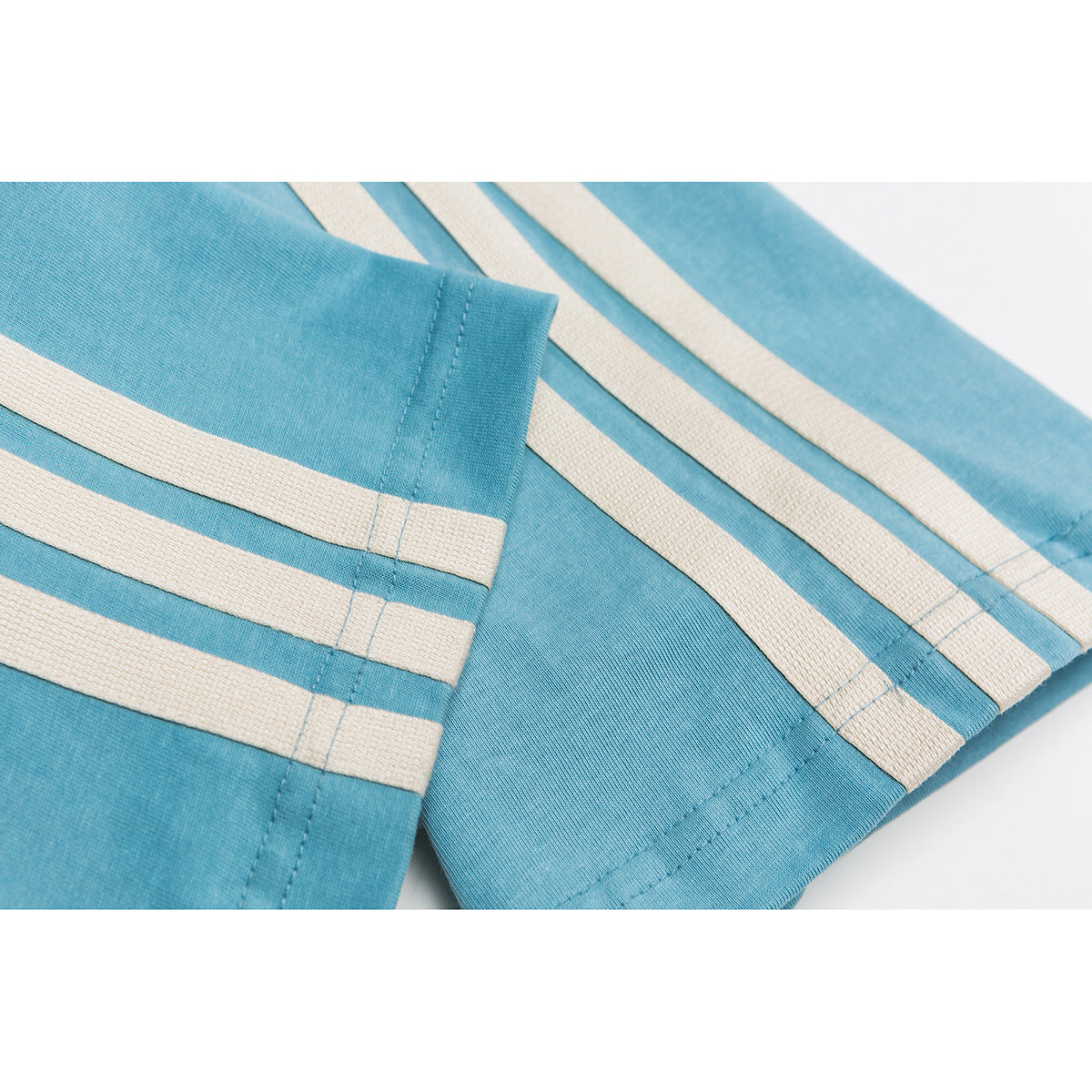 Close-up of turquoise T-shirt fabric with cream parallel stripes and stitched sleeve and hem edges.
