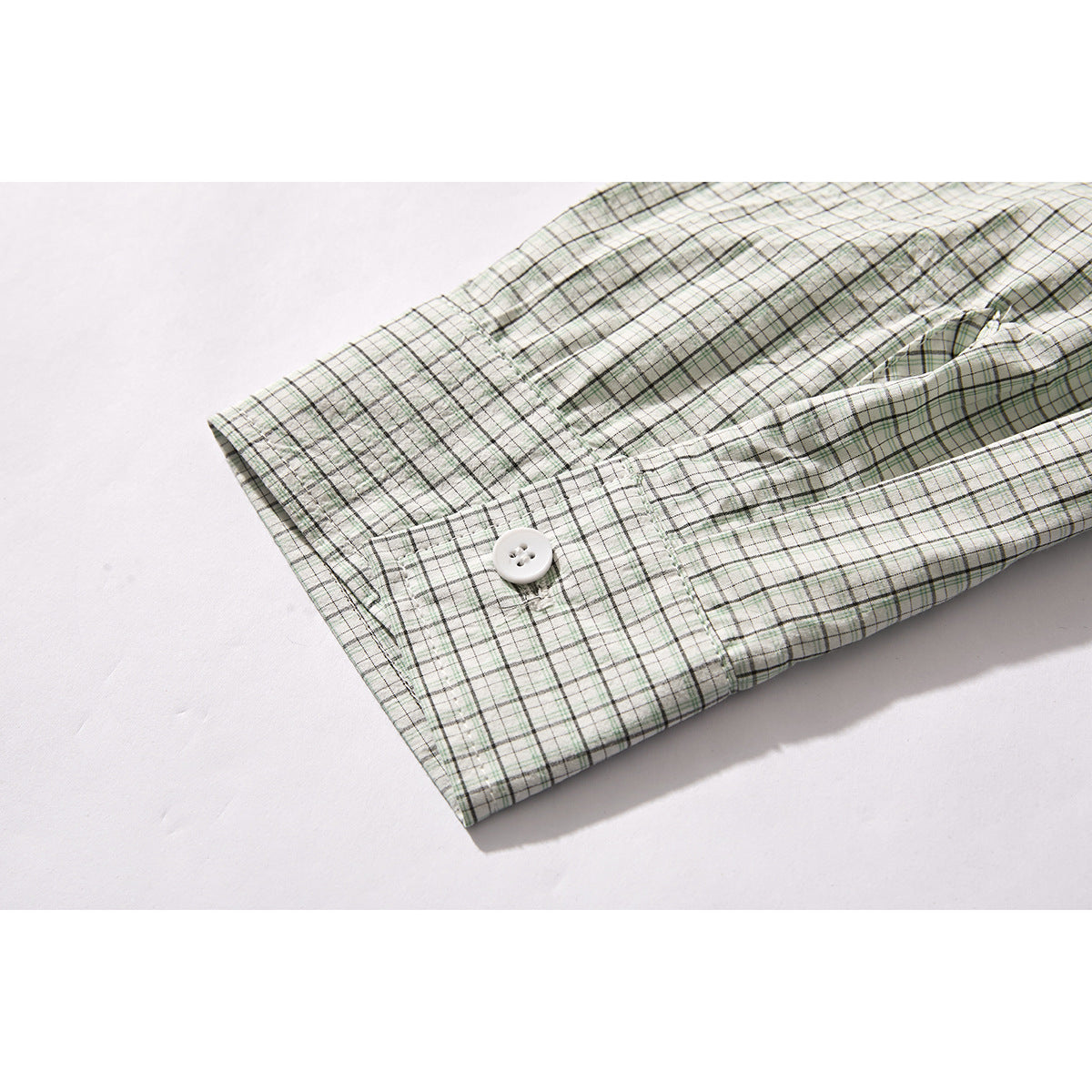 Close-up of the buttoned cuff and sleeve of a pale green and gray plaid shirt.