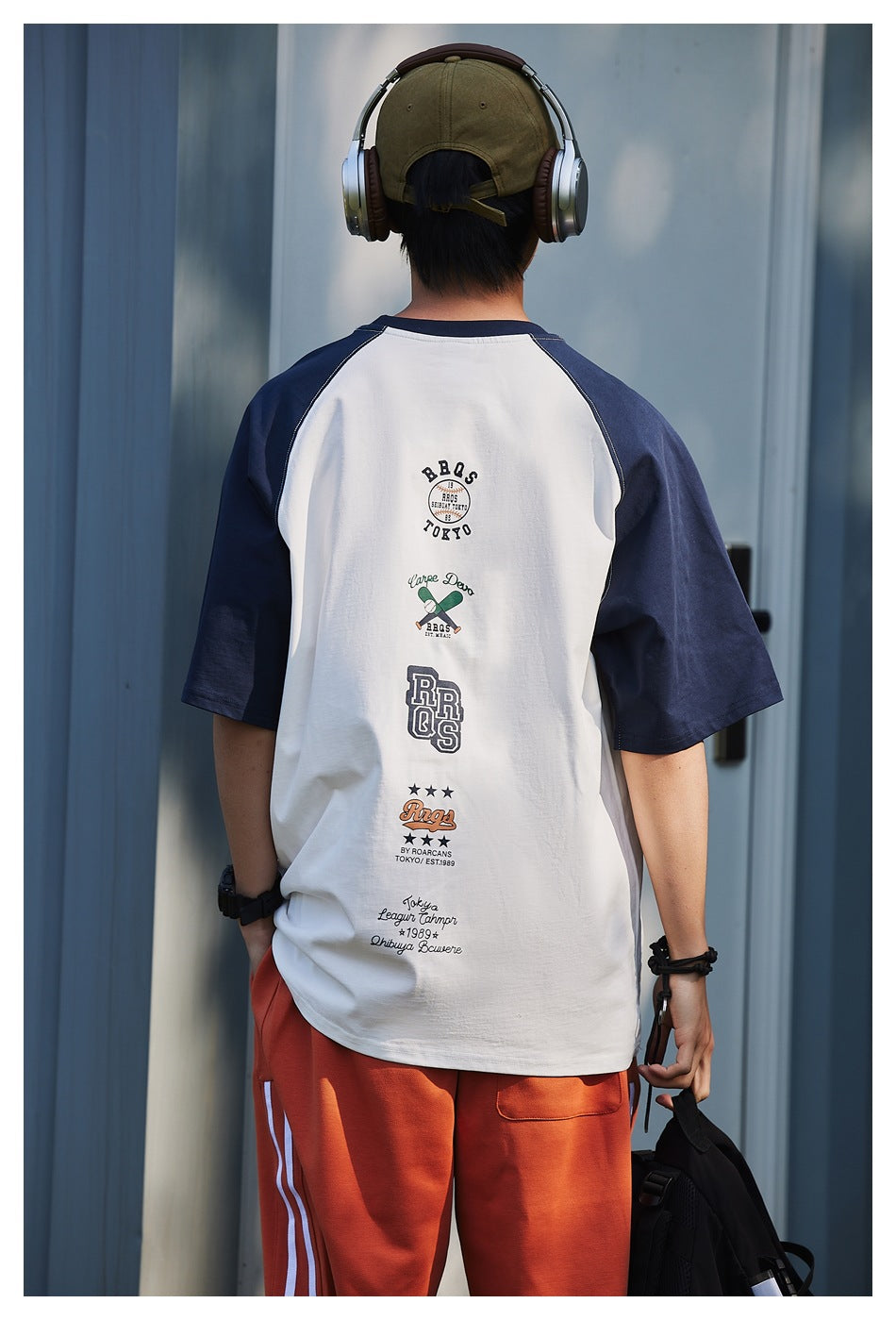 Back view of a model wearing a white T-shirt with navy raglan sleeves and a column of graphics down the back.