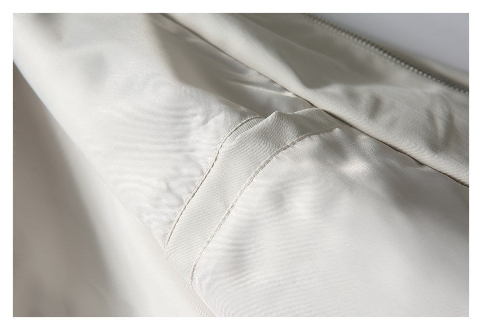 Close-up of an off-white garment showing a curved stitched seam beside a metal zipper.