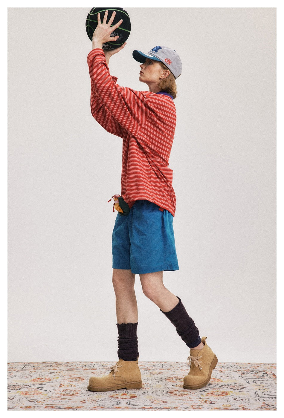 Side view of a person in a red striped long-sleeve top and blue shorts raising a basketball overhead