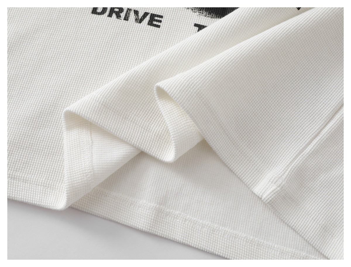 Close-up of a white waffle-knit shirt folded to show its stitched hem and a partial black chest graphic.