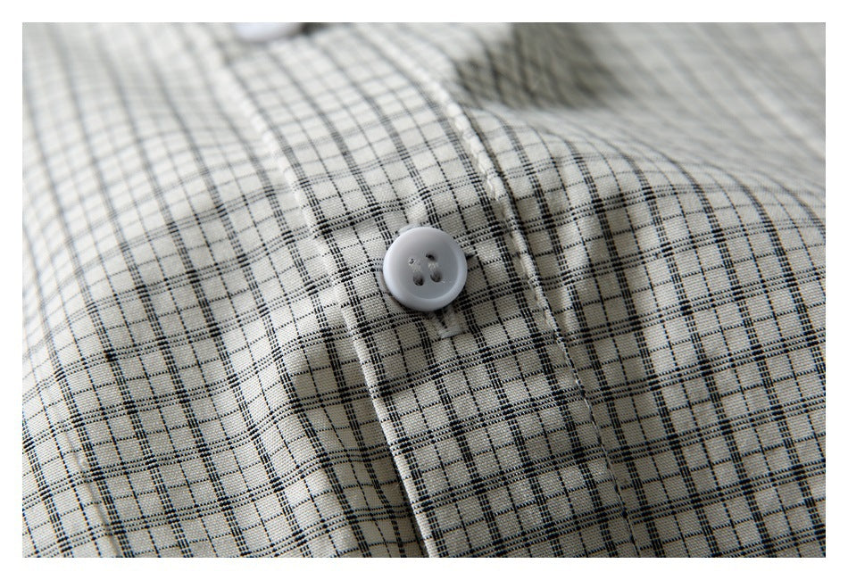 Close-up of a white button and stitching on the fine black and gray check fabric of an off-white shirt.