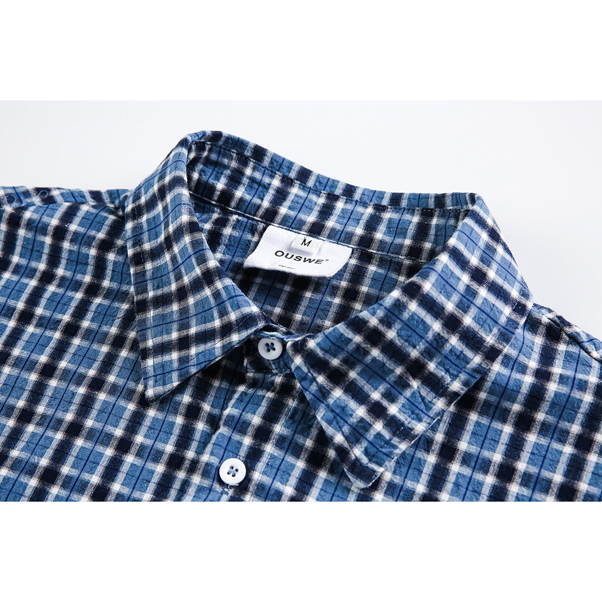 Close-up of a blue, black, and white plaid shirt collar, buttons, and sewn neck label.