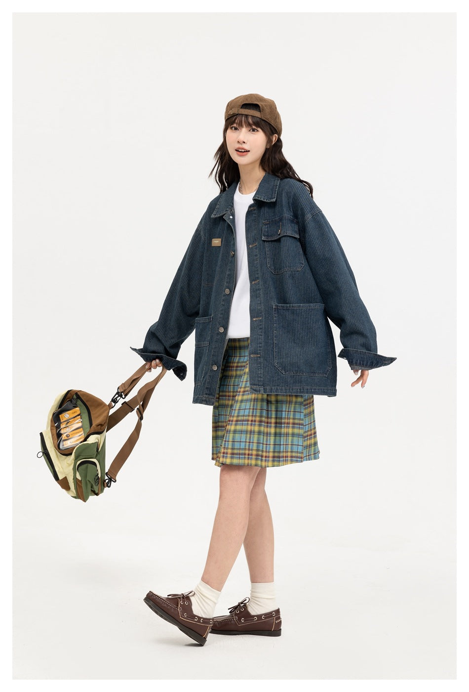 Model wearing a dark blue denim jacket with roomy pockets over a white top and plaid skirt.