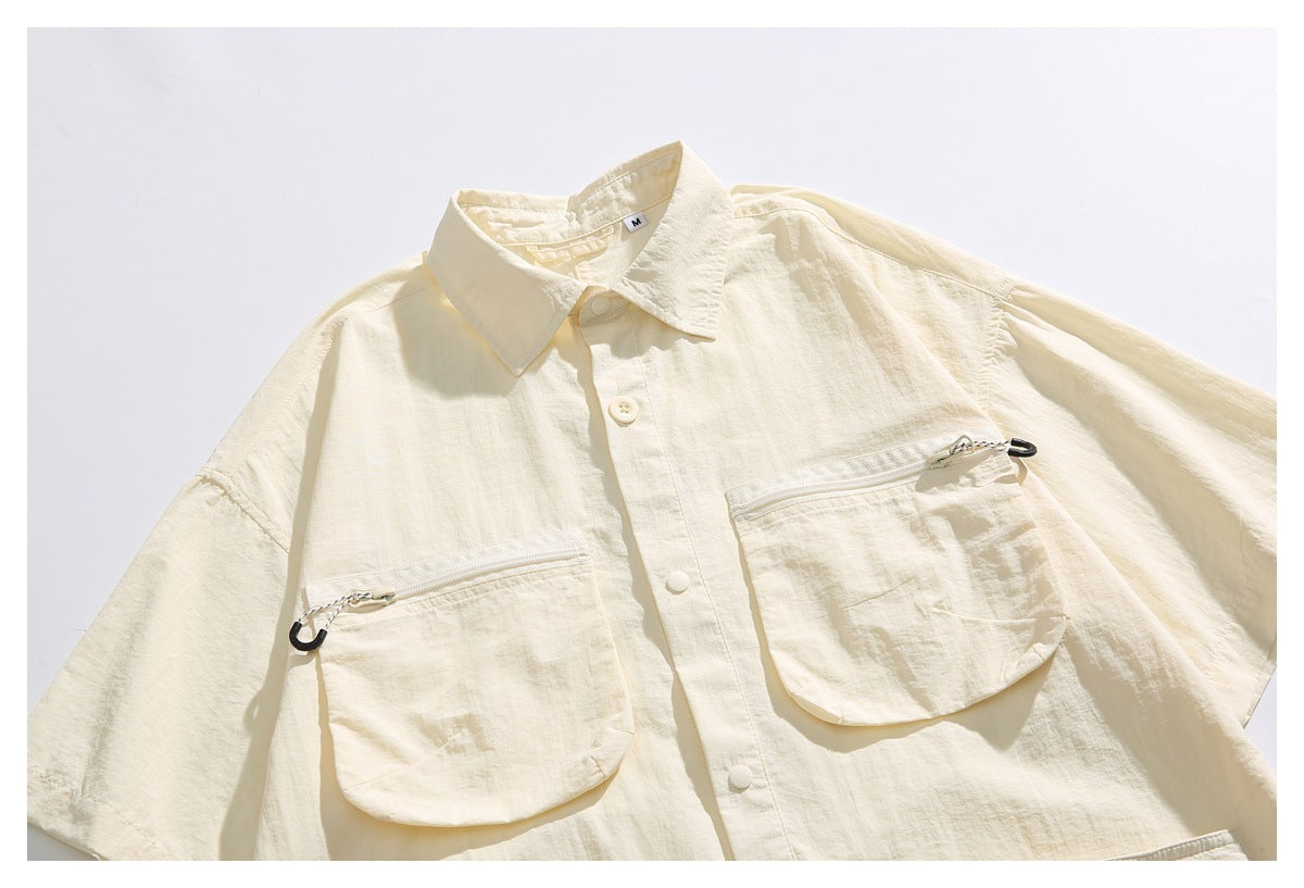 Close-up of an ivory short-sleeve shirt with two large chest pockets, horizontal zippers, and snap buttons.