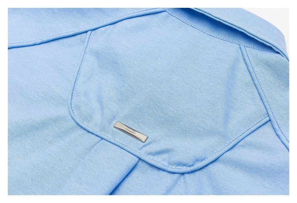 Close-up of a pale blue shirt pocket with a small metal emblem.