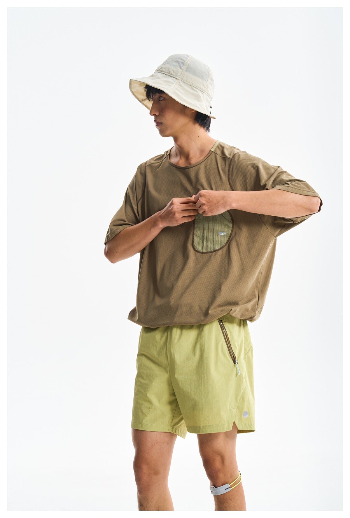 Model demonstrates the shirt's chest pocket while wearing a brown T-shirt and light yellow-green shorts.
