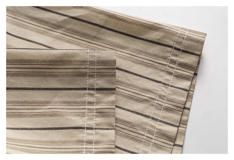 Close-up of a beige shirt hem with narrow brown and dark gray stripes and parallel white stitching.