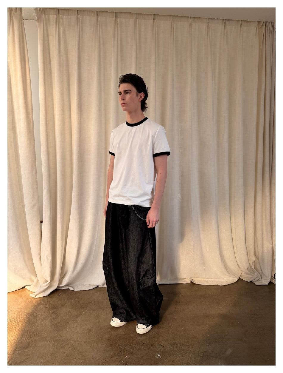 Model wearing a white T-shirt with black collar and cuff trim, front view, with wide dark cargo jeans