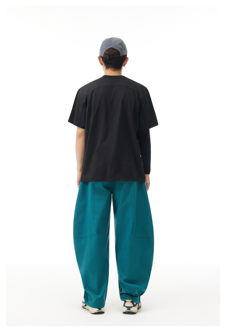 Back view of a model wearing a black short-sleeve shirt and loose teal pants.