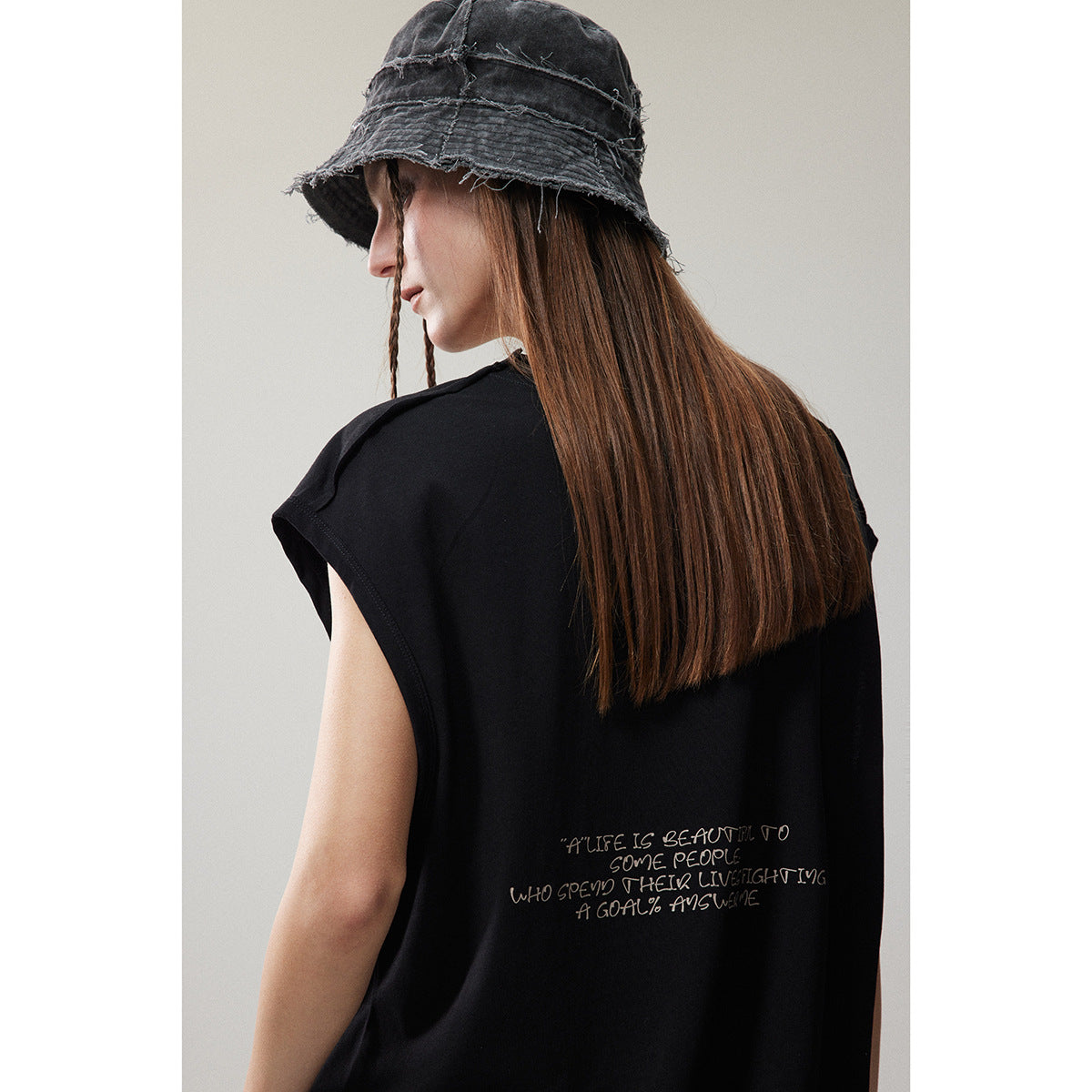 Back view of a model wearing a black sleeveless top with a handwritten-style quote printed near the hem.