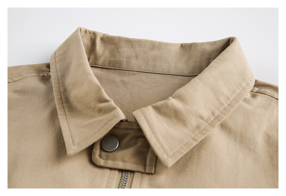 Close-up of a tan jacket's pointed collar, metal snap, and front zipper.