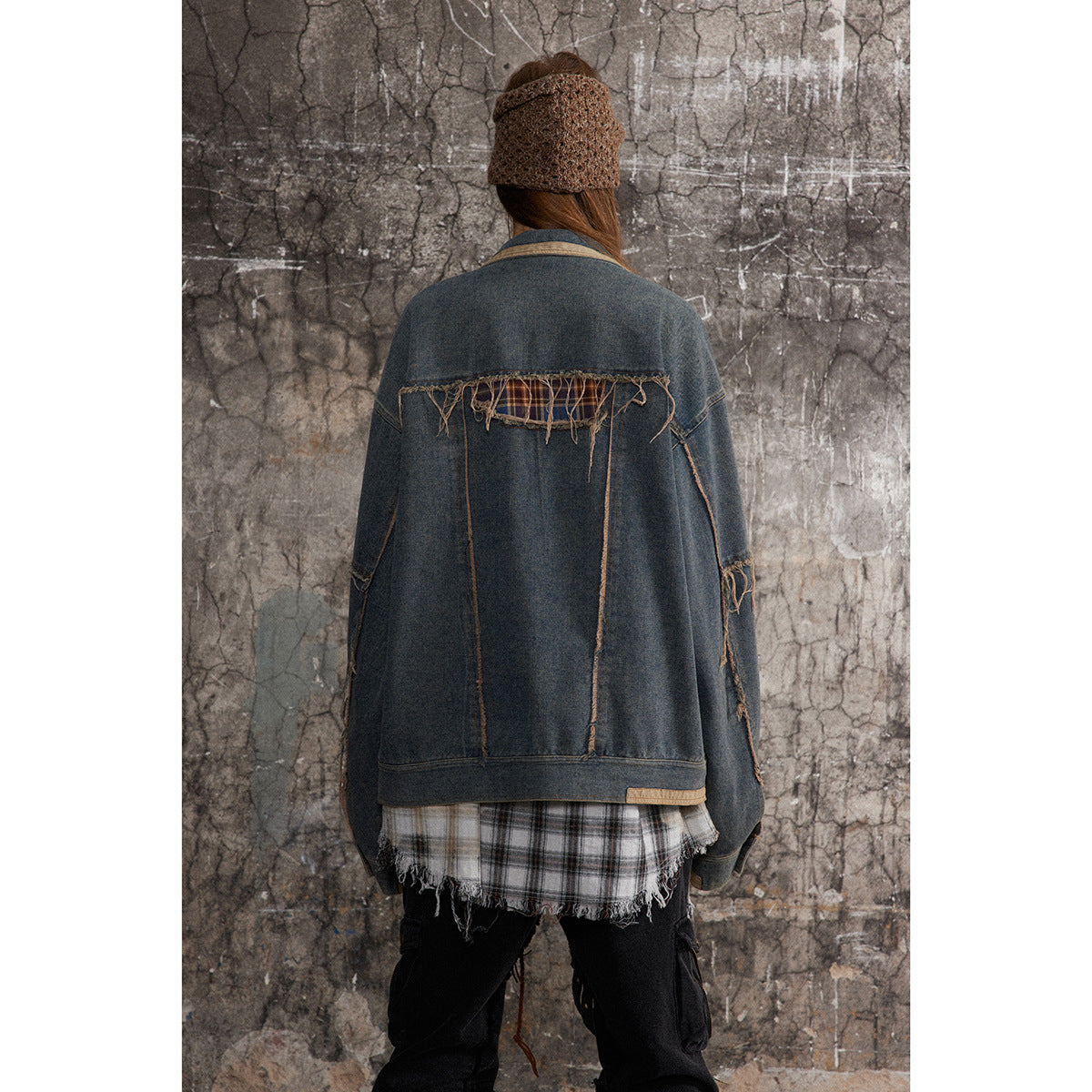 Back view of a model wearing an oversized blue denim jacket with a frayed plaid insert across the shoulders.