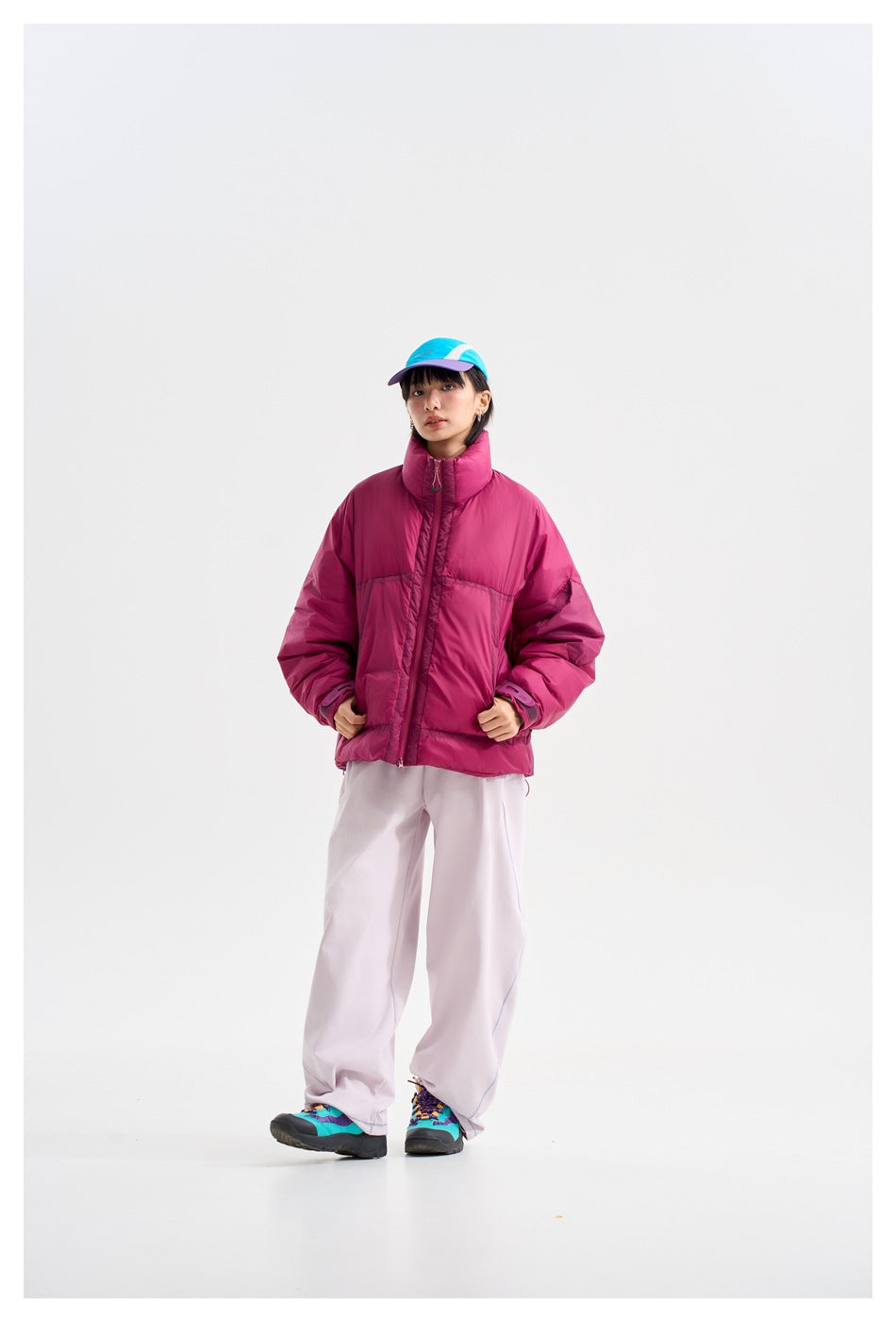 Model wearing a magenta high-collar puffer jacket and pale wide-leg trousers, standing with one foot forward.