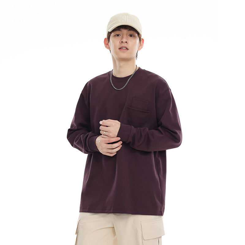 Model wearing a dark plum long-sleeve crewneck shirt with a chest pocket and cream cap.