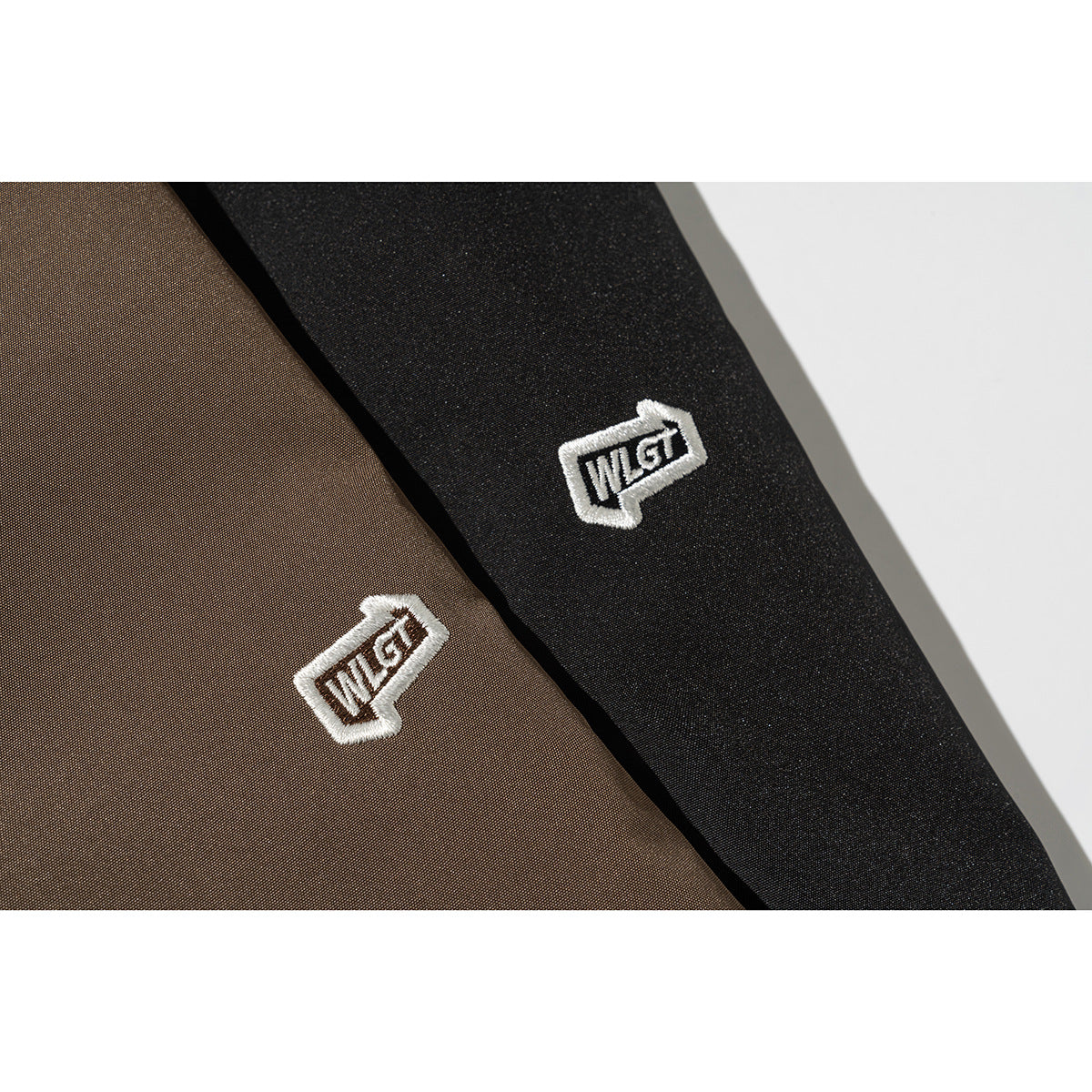 Close-up of white embroidered logos on brown and black jacket fabric.