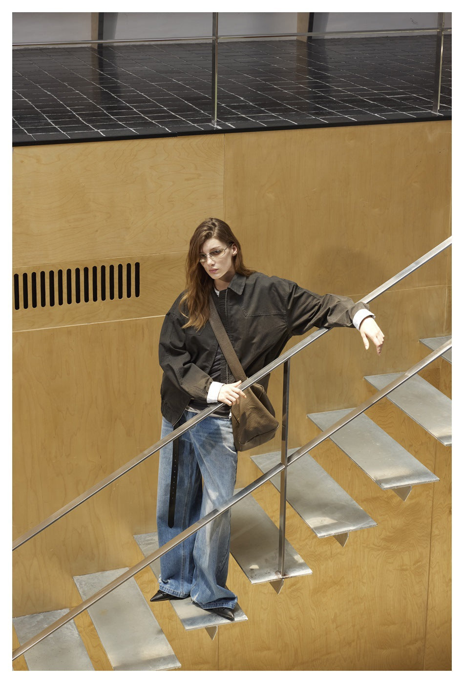 Model wearing an oversized charcoal collared jacket with checked cuffs and wide-leg blue jeans on a staircase.