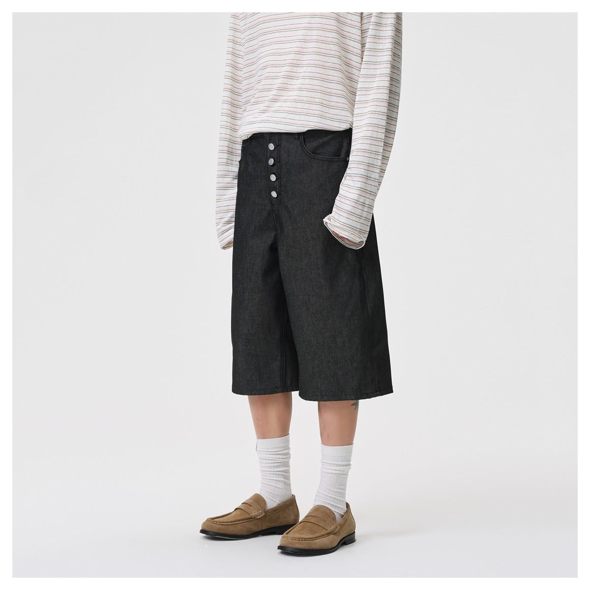 Side-angle view of model wearing black wide-leg knee-length shorts with striped top, white socks and suede loafers