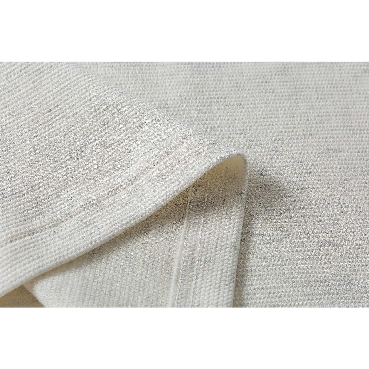 Close-up of the off-white shirt's stitched hem and overlocked seam.