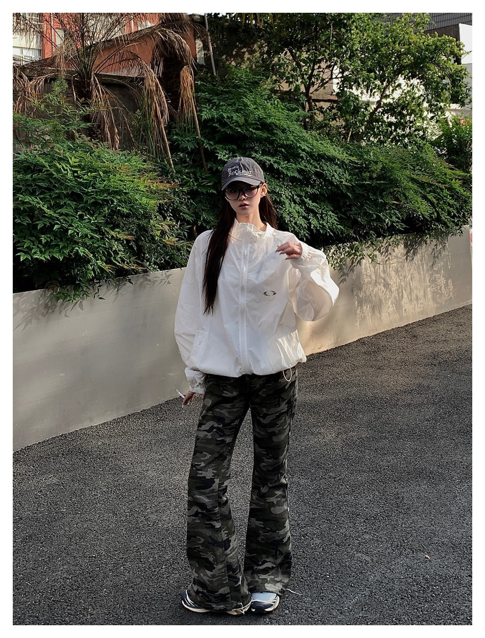 Model wearing a white zip-front stand-collar jacket with camouflage flared pants and a gray cap outdoors
