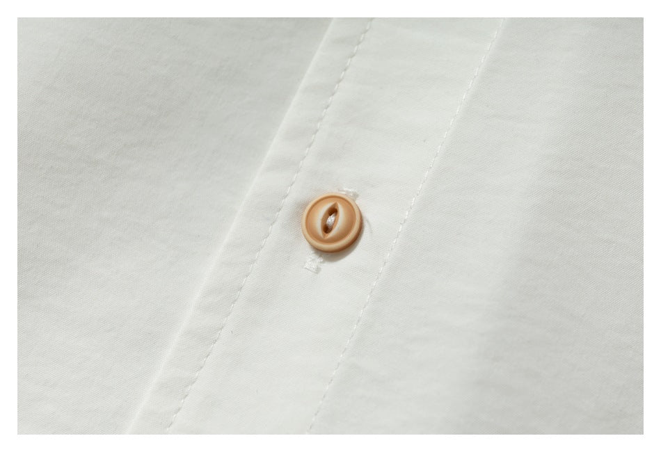 Close-up of a tan button and stitched placket on off-white fabric.