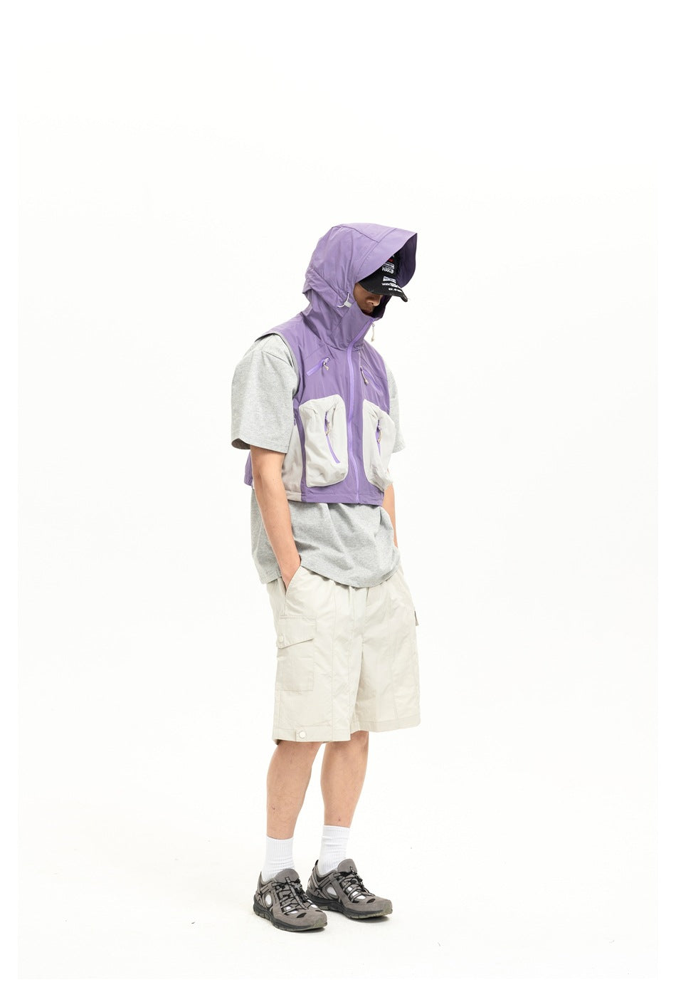 Model wearing a lavender and light gray hooded utility vest with cream shorts and a gray T-shirt.
