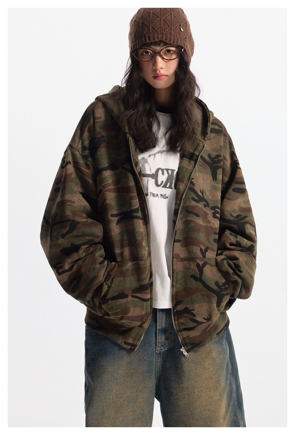 Front view of a model wearing an oversized camouflage zip hoodie over a white graphic tee.