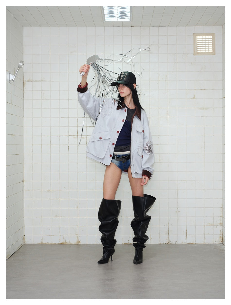 Model wearing a pale gray jacket with a dark brown collar and red buttons, denim shorts, and tall black boots.