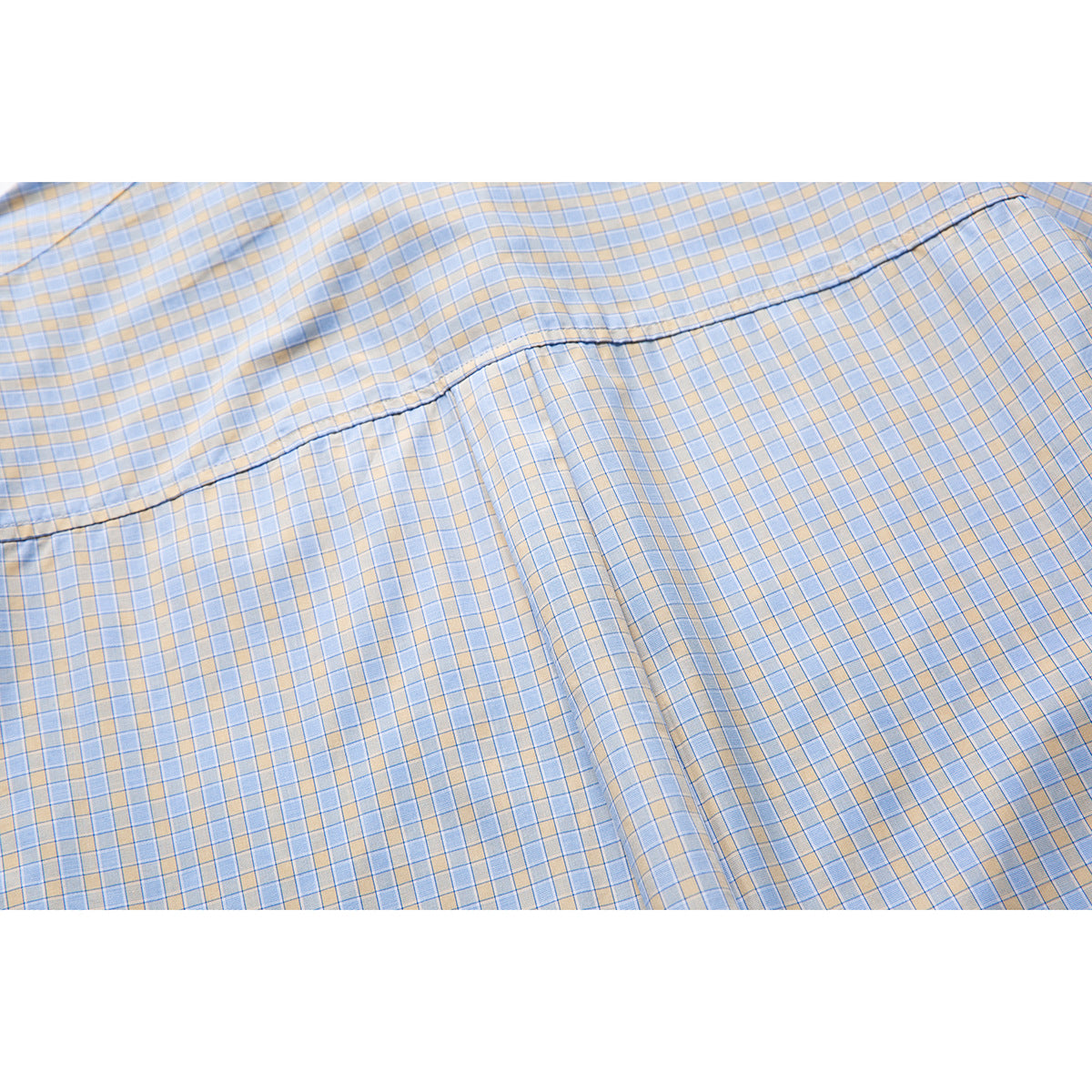 Close-up of a curved stitched seam on light blue and beige plaid shirt fabric.
