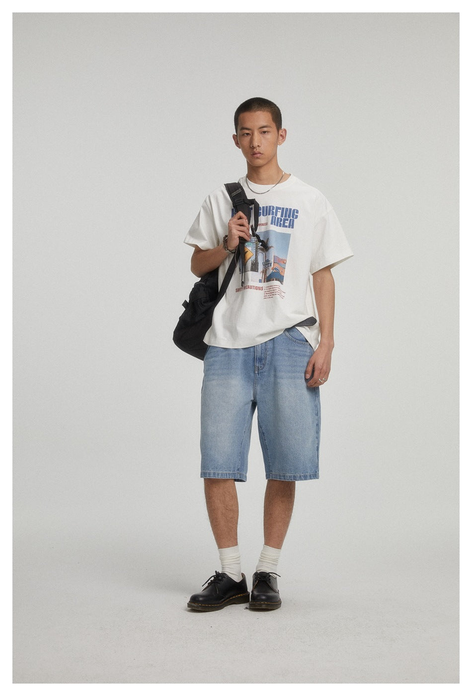 Model in a white printed T-shirt and light blue denim shorts, carrying a black shoulder bag.