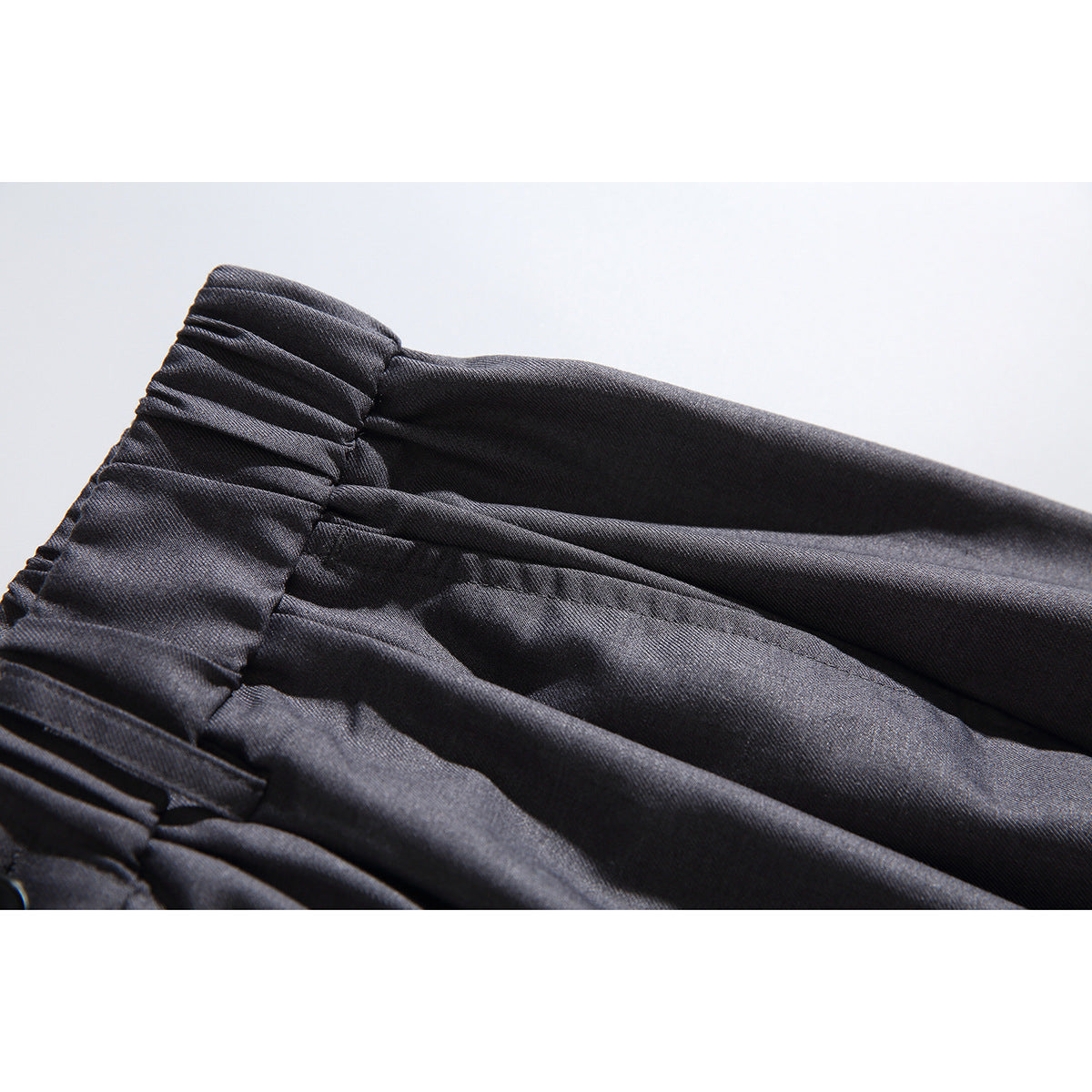 Close-up of the gathered elastic waistband and pleats on charcoal-gray trousers.