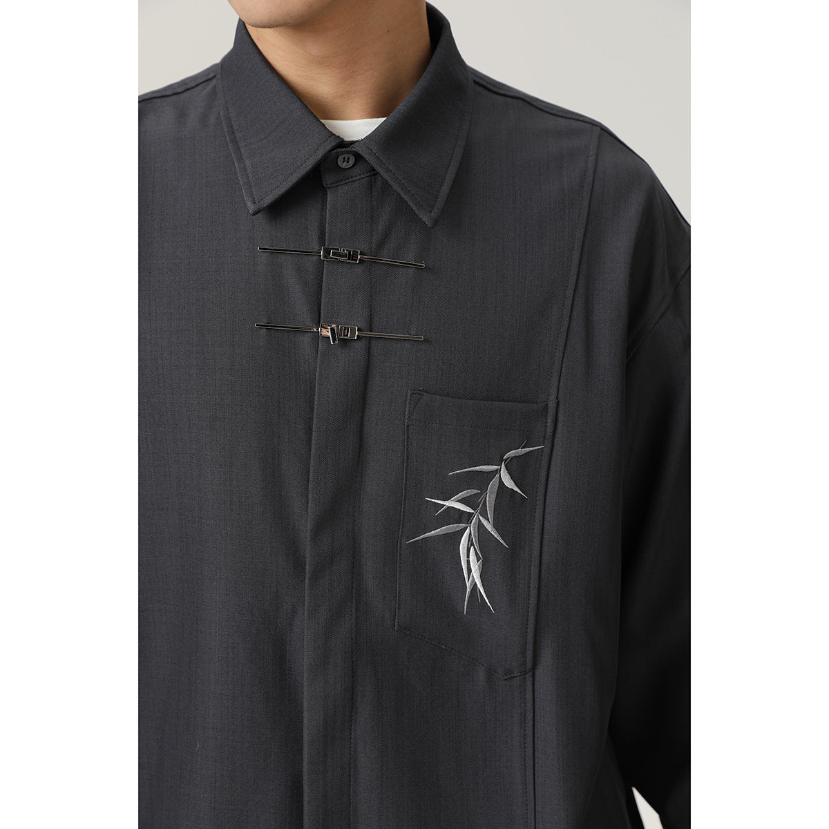 Close-up of the charcoal shirt’s pointed collar, metal front fasteners, and bamboo embroidery on the chest pocket.