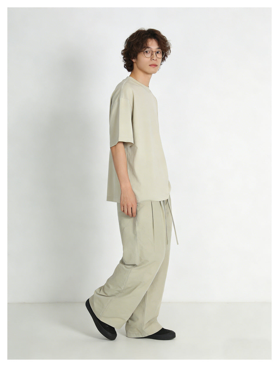 Model wearing a light beige T-shirt and wide-leg drawstring trousers, shown in side view.