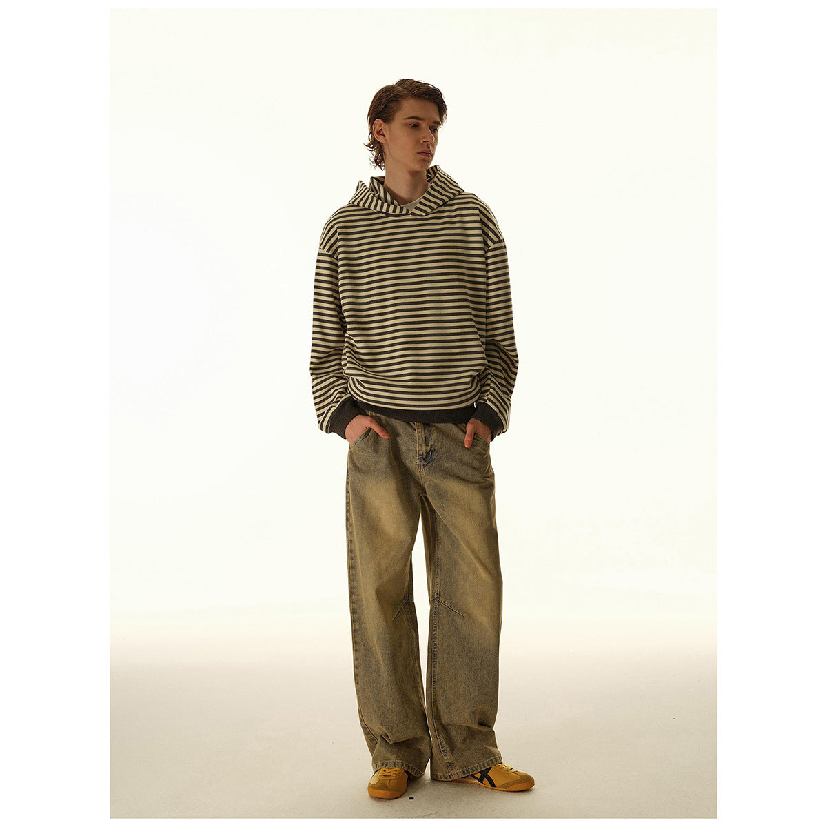Model wearing a loose beige and dark striped hooded sweatshirt with dark ribbed cuffs and hem, viewed from the front.
