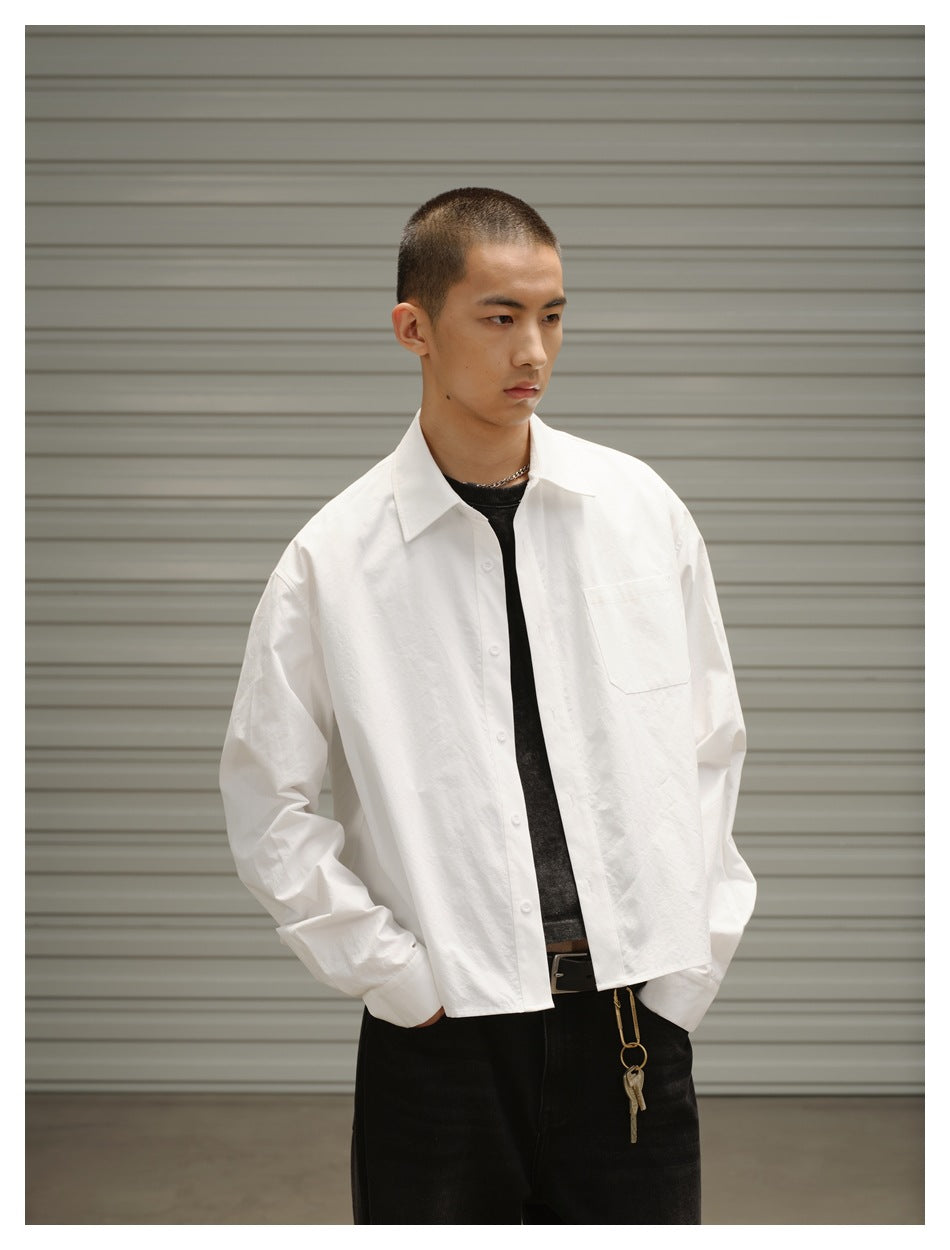 Model in a white cropped button-up shirt worn open over a dark tee, hands in pockets, close-up of collar and chest pocket