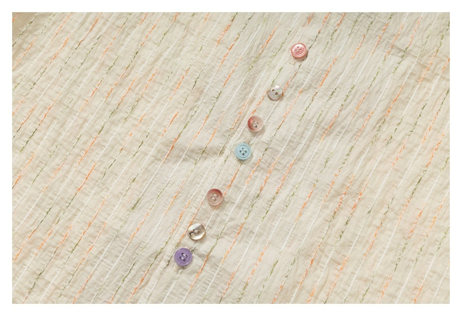 Close-up of the ivory shirt's textured, striped fabric and placket with assorted pastel buttons.