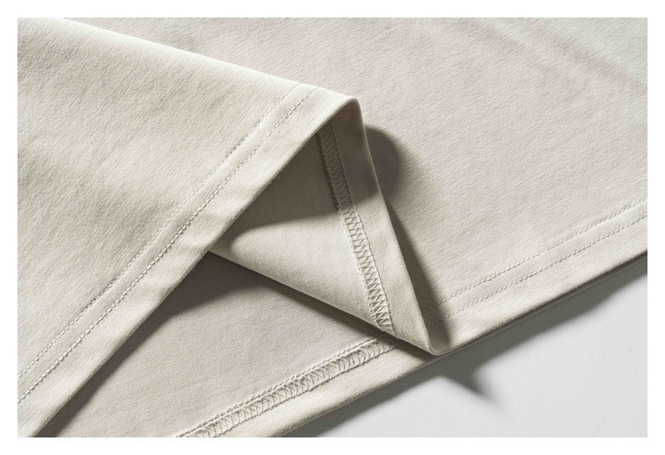 Close-up of a light beige T-shirt's folded hem, showing the stitching and inside seam.