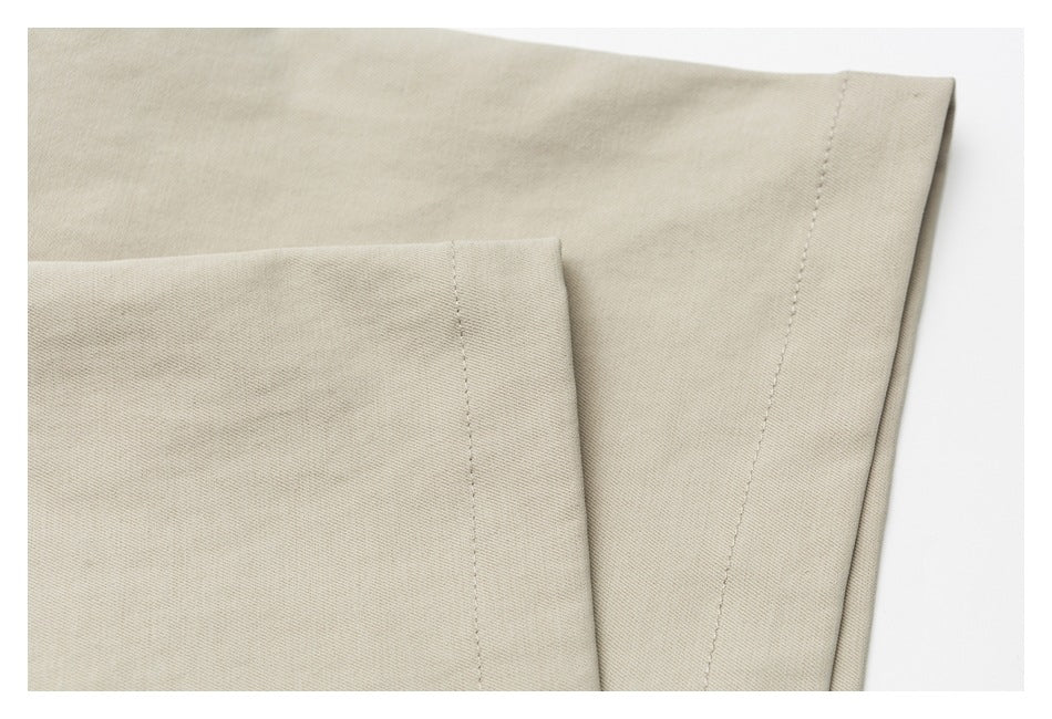 Close-up of beige garment fabric showing a folded edge and parallel stitched seams.