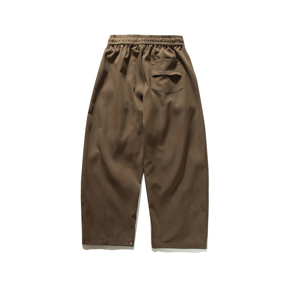 Back view of loose brown trousers with an elastic waist and a patch pocket.