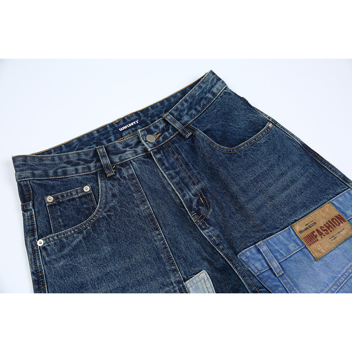 Close-up of dark blue patchwork jeans showing the front waistband, button, pockets, and a light blue denim panel.