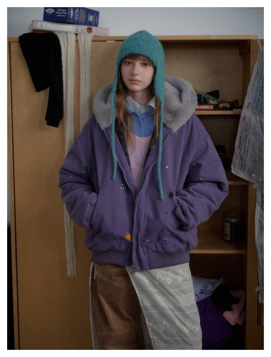 Front view of a model wearing a purple zip jacket with a gray plush collar and scattered paint-like marks.