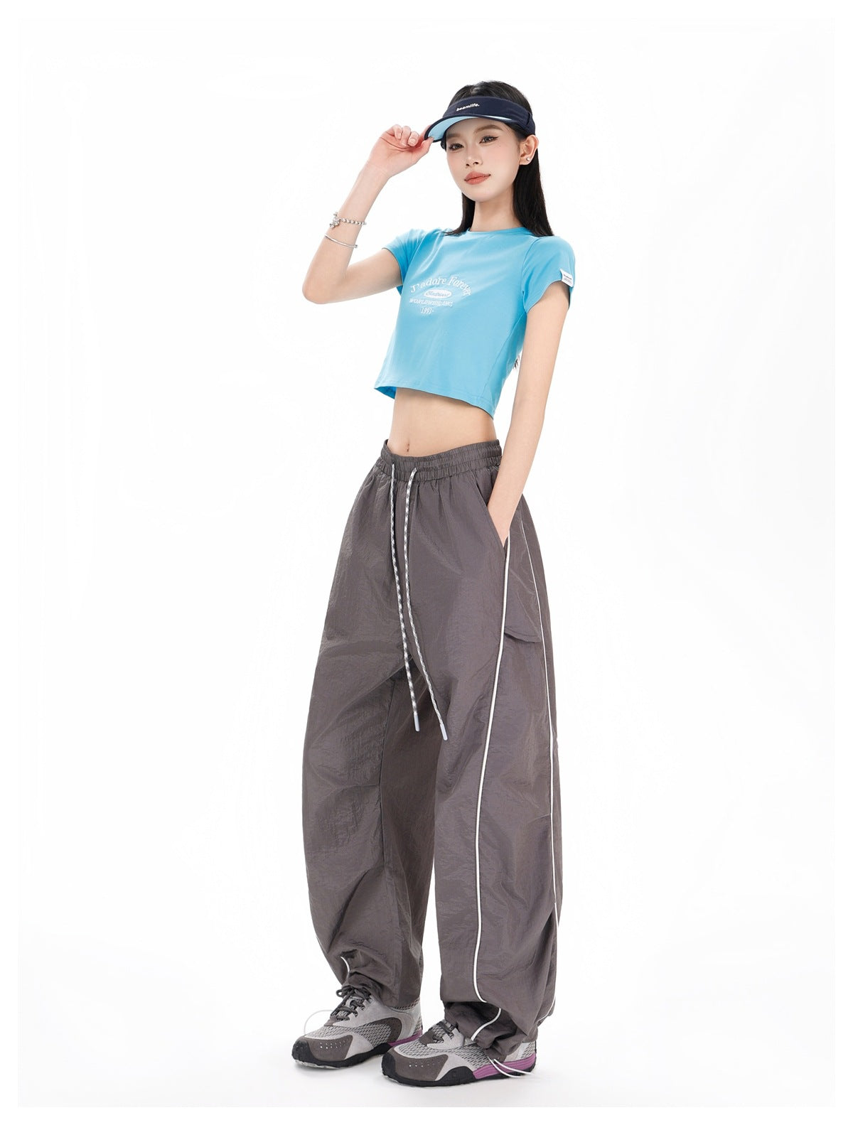 Angled full-length view of a model wearing charcoal-gray wide-leg pants with white piping and a blue cropped T-shirt.